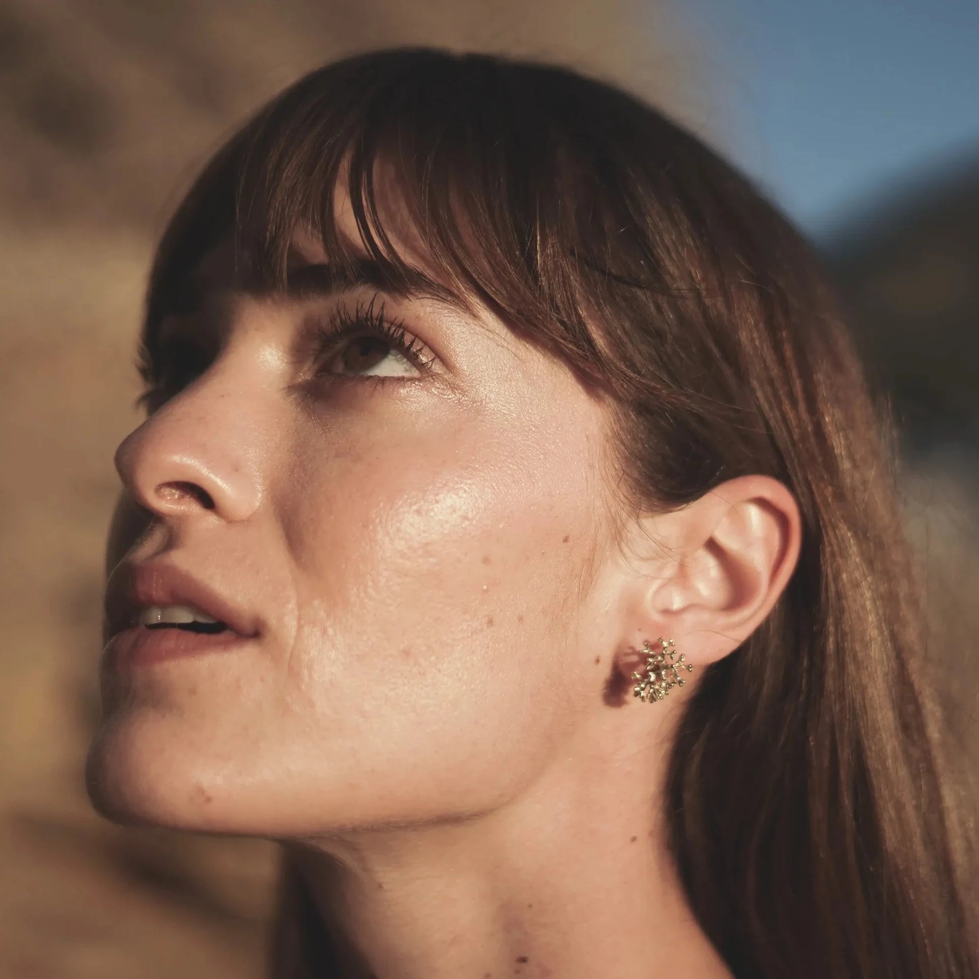 Modelo morena mirando al cielo con los pendientes de Coralina bañados en Oro en la oreja.